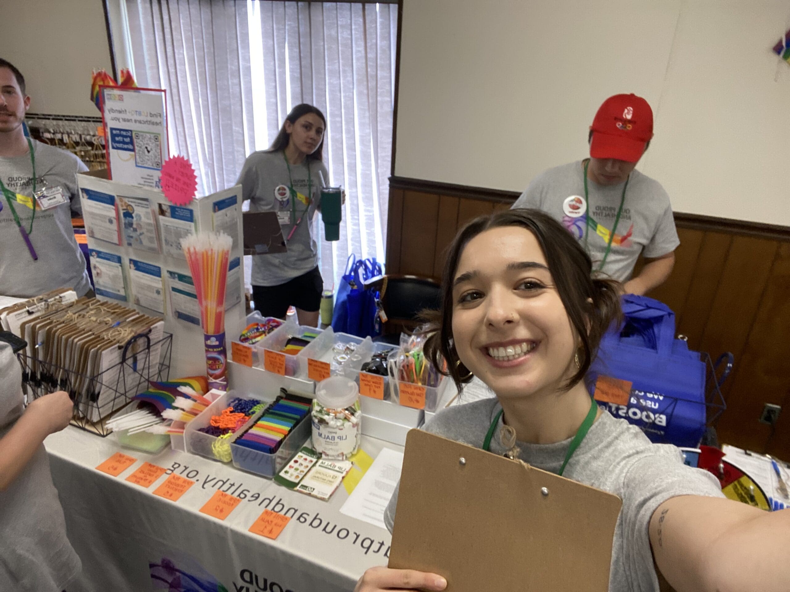 Out, Proud, and Healthy employees smile while working at a booth.