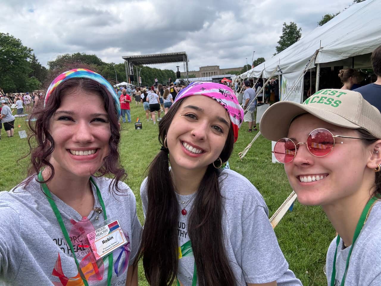 Out, Proud, and Healthy employees smile in front their pride fest booth.